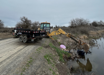 A tractor removing refuse dumped on the edge of wetlands